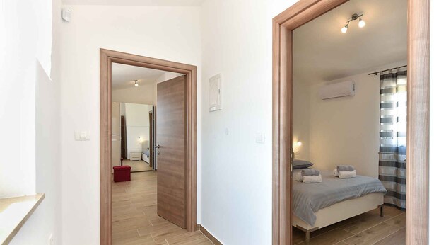 A modern hotel room with a wooden floor, a bed with a grey bedspread, and a window with striped curtains. - Villa with swimming pool and table tennis (Divšići)