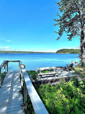 A wooden dock leading to a beach with a picnic table and chairs, surrounded by greenery. - Waterfront Getaway Near Acadia w/ Spectacular View (Deer Isle)