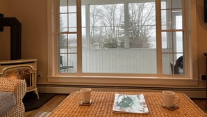 Ein gemütliches Zimmer mit einem großen Fenster, einem Kamin und zwei Tassen auf einem gewebten Tisch.