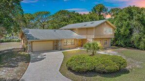 A two-story house with a garage, a covered driveway, and a well-maintained lawn. - Behind Closes Doors just 4.5 miles away from the beach! (Vero Beach)