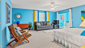 A room with a bed, a sofa, a rocking chair, a TV, and a ceiling fan. - Behind Closes Doors just 4.5 miles away from the beach! (Vero Beach)