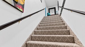 A carpeted staircase with metal handrails, leading to a door with a blue object on the landing. - Behind Closes Doors just 4.5 miles away from the beach! (Vero Beach)