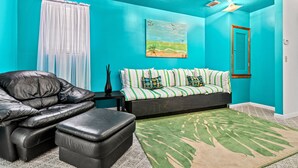 A room with teal walls, a black leather sofa, a green patterned rug, and a painting of a beach scene. - Behind Closes Doors just 4.5 miles away from the beach! (Vero Beach)