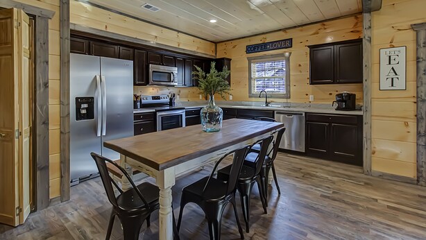 A kitchen with wooden walls, a stainless steel refrigerator, a wooden dining table with four chairs, and a sign that says "Coffee Lover".