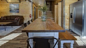 A wooden dining table with chairs, a vase with greenery, and a stainless steel refrigerator in a cabin-style interior.
