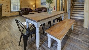 A wooden dining table with benches, a brown leather sofa, and a vase with flowers.