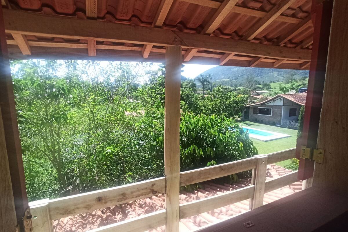 Un balcón de madera con vista a una piscina y abundante vegetación.