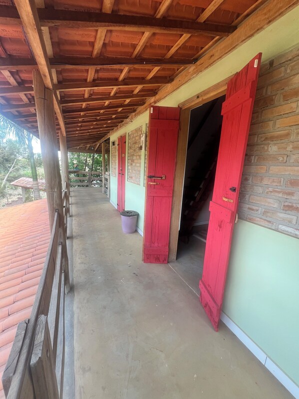 A covered outdoor area with a concrete floor, wooden beams, and red doors. - Pousada Rural Rancho do Marçal (Santa Rita do Sapucai)