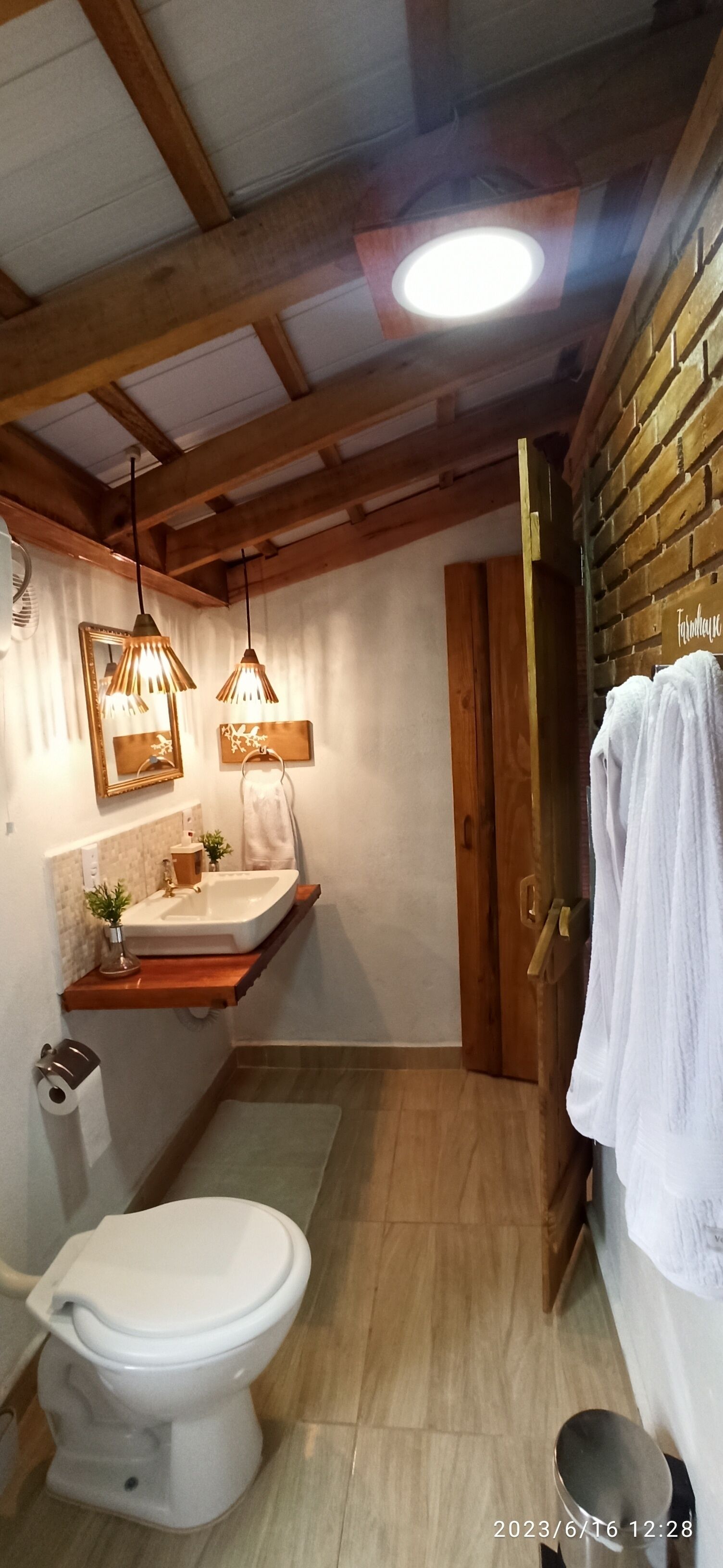 A bathroom with a wooden ceiling, a white sink, a toilet, and a towel rack.