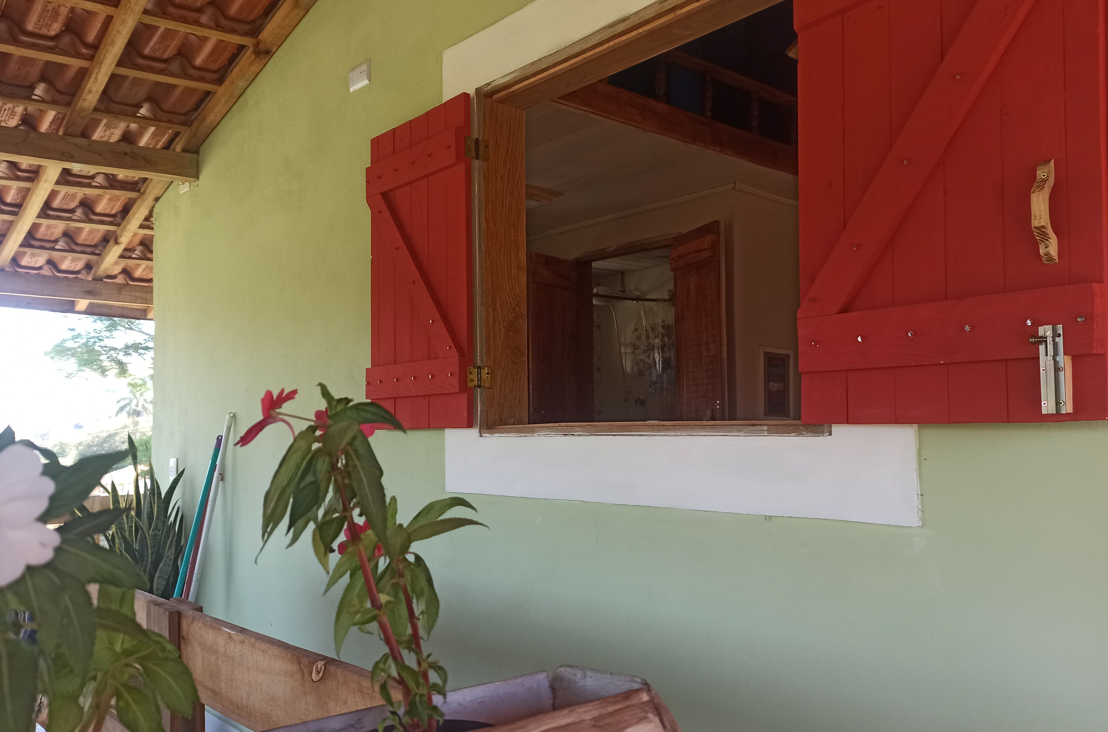 A room with a green wall, a wooden ceiling, and red shutters on the window.