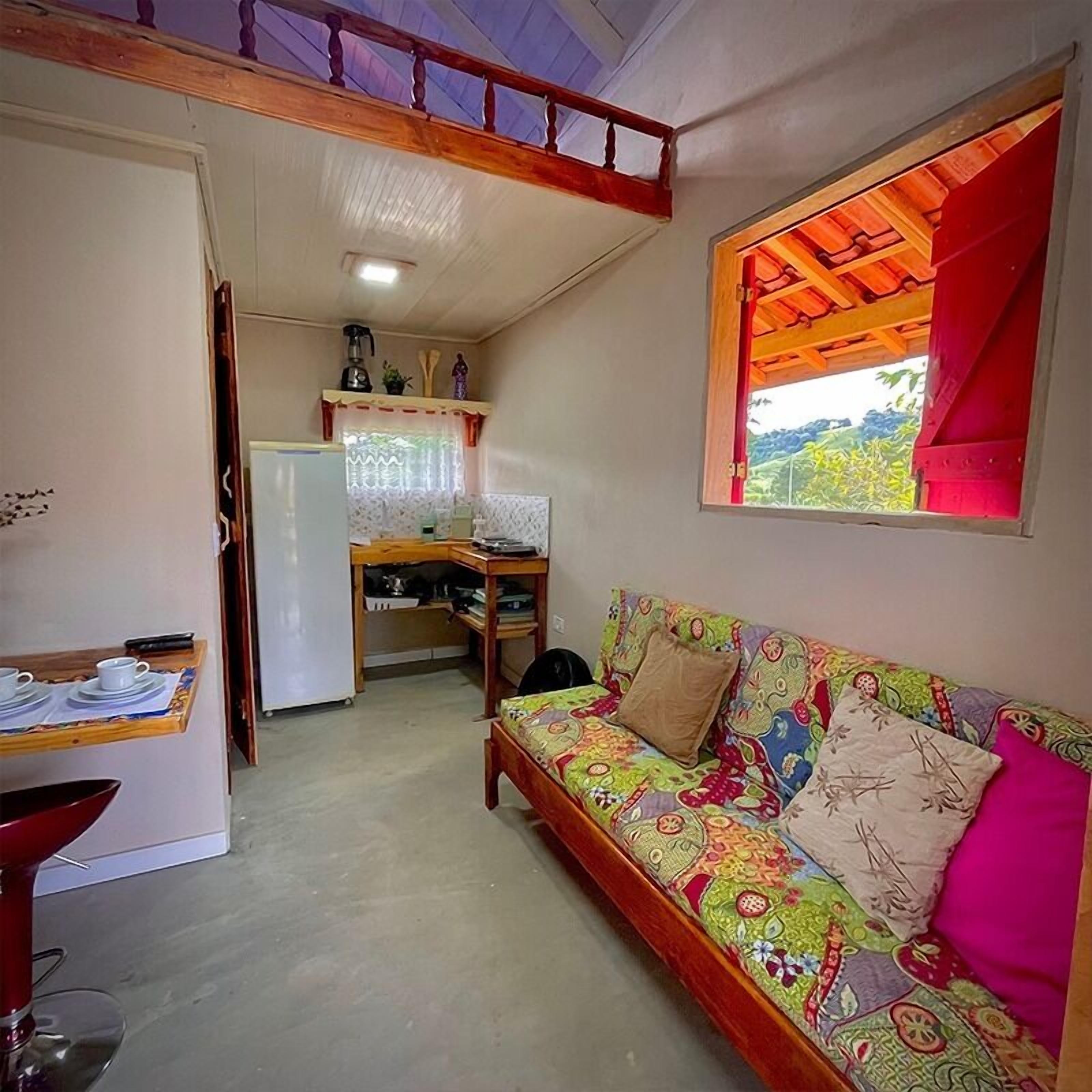 A compact living space with a kitchenette, a sofa with colorful cushions, and a window with a red curtain.