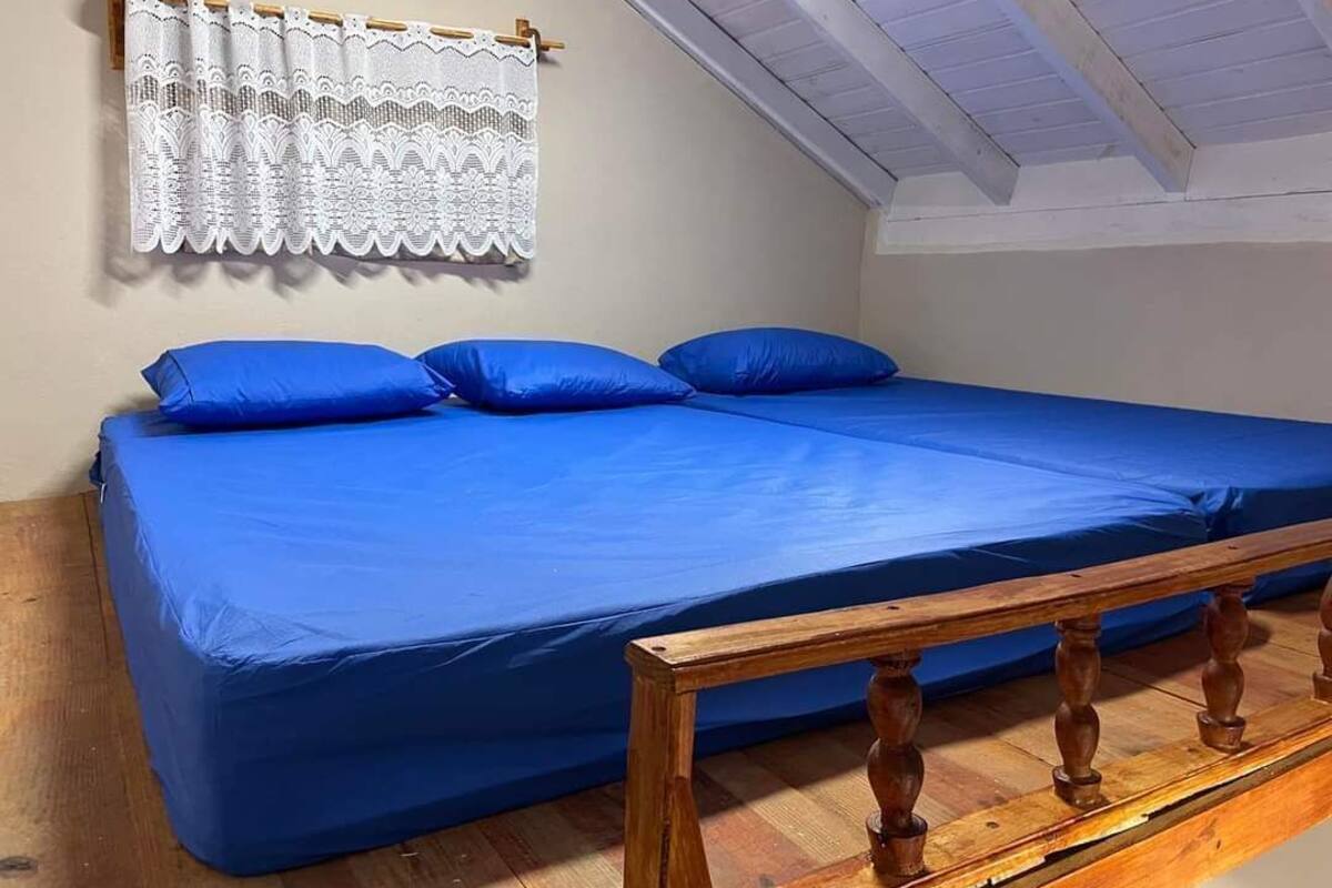 Habitación individual con una cama de madera, un cabezal de madera, cortina de encaje y techo inclinado.