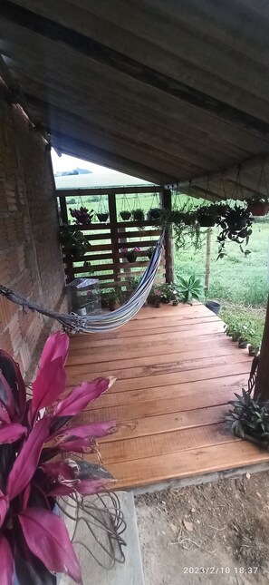 A wooden deck with a hammock, potted plants, and a view of a grassy field.