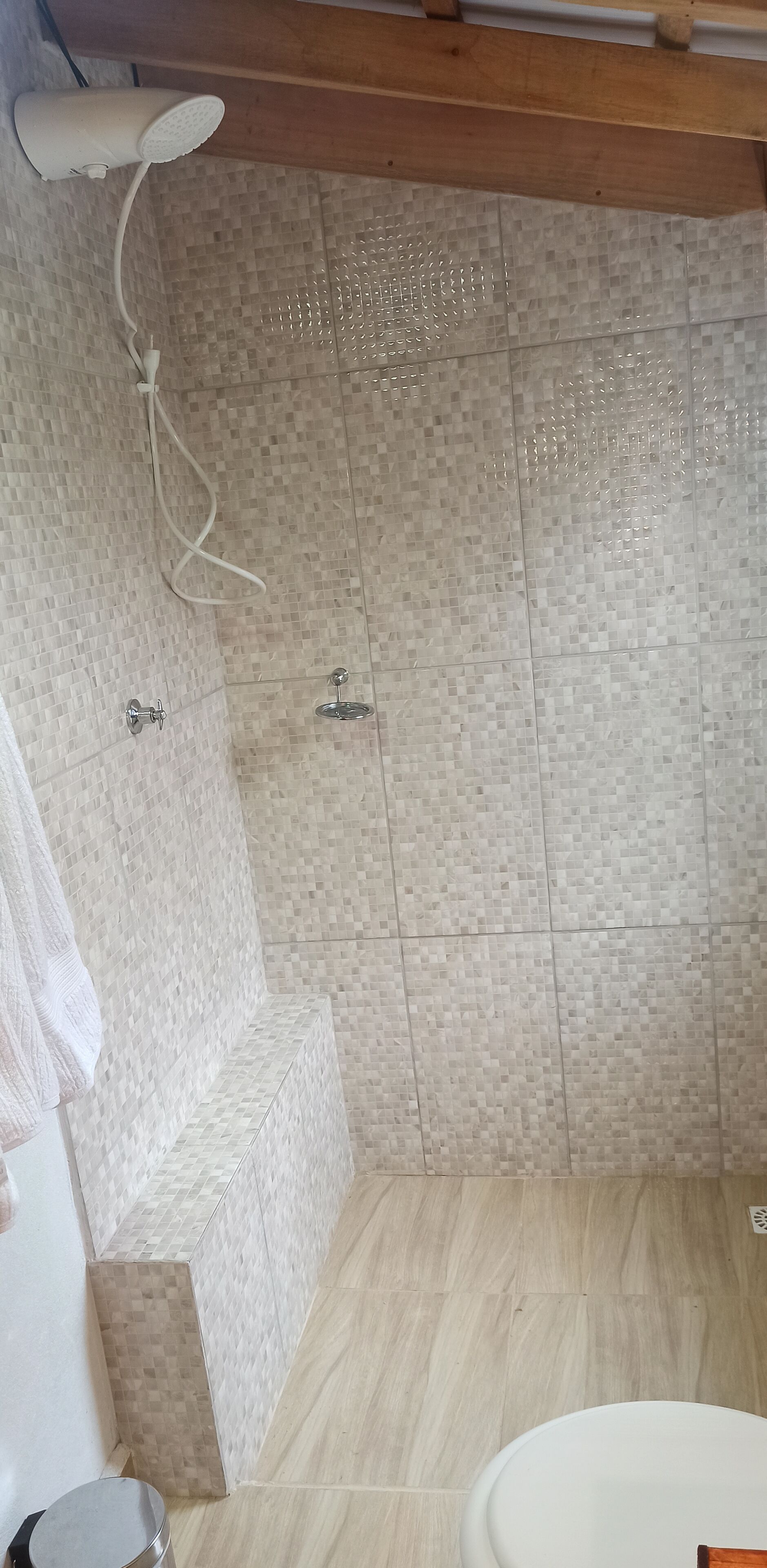 Casa de banho com chuveiro, paredes revestidas a azulejo, teto de madeira e sanita branca.