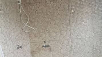 Casa de banho com chuveiro, paredes revestidas a azulejo, teto de madeira e sanita branca.