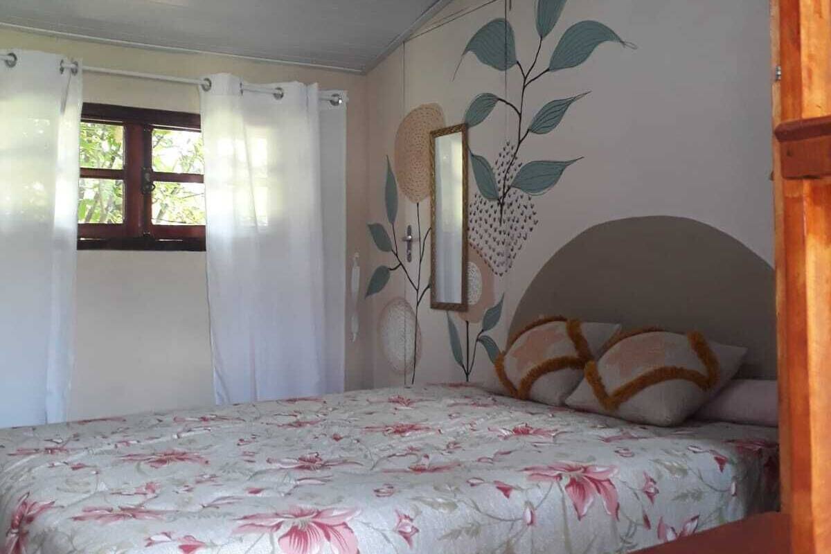 Un dormitorio con cama, ventana con cortinas, pared con un mural de hojas y cabecera de madera.