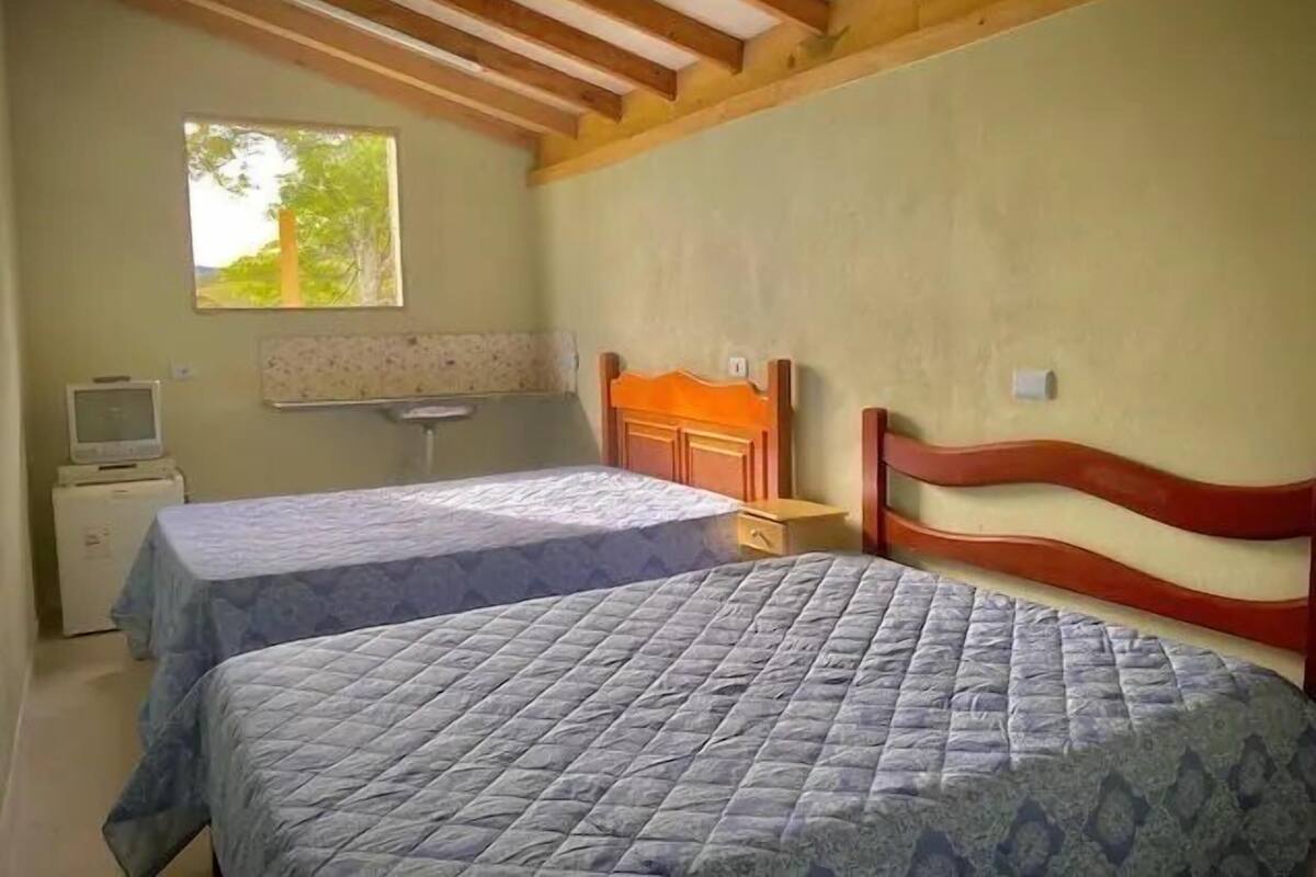 Un dormitorio con dos camas, techo de madera, una ventana y un pequeño televisor sobre un mueble.