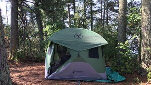 A Gazelle tent set up in a forested area with trees and a dirt ground.