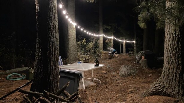 A campsite with string lights, a table, and a bottle.