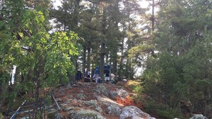 A campsite with a tent, a portable toilet, and a rocky terrain surrounded by trees.