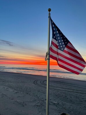 Eine amerikanische Flagge an einem Fahnenmast am Strand bei Sonnenuntergang.