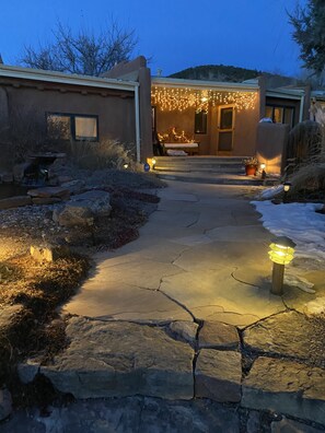 A stone pathway leading to a house with a porch decorated with string lights, a small bench, and a potted plant.