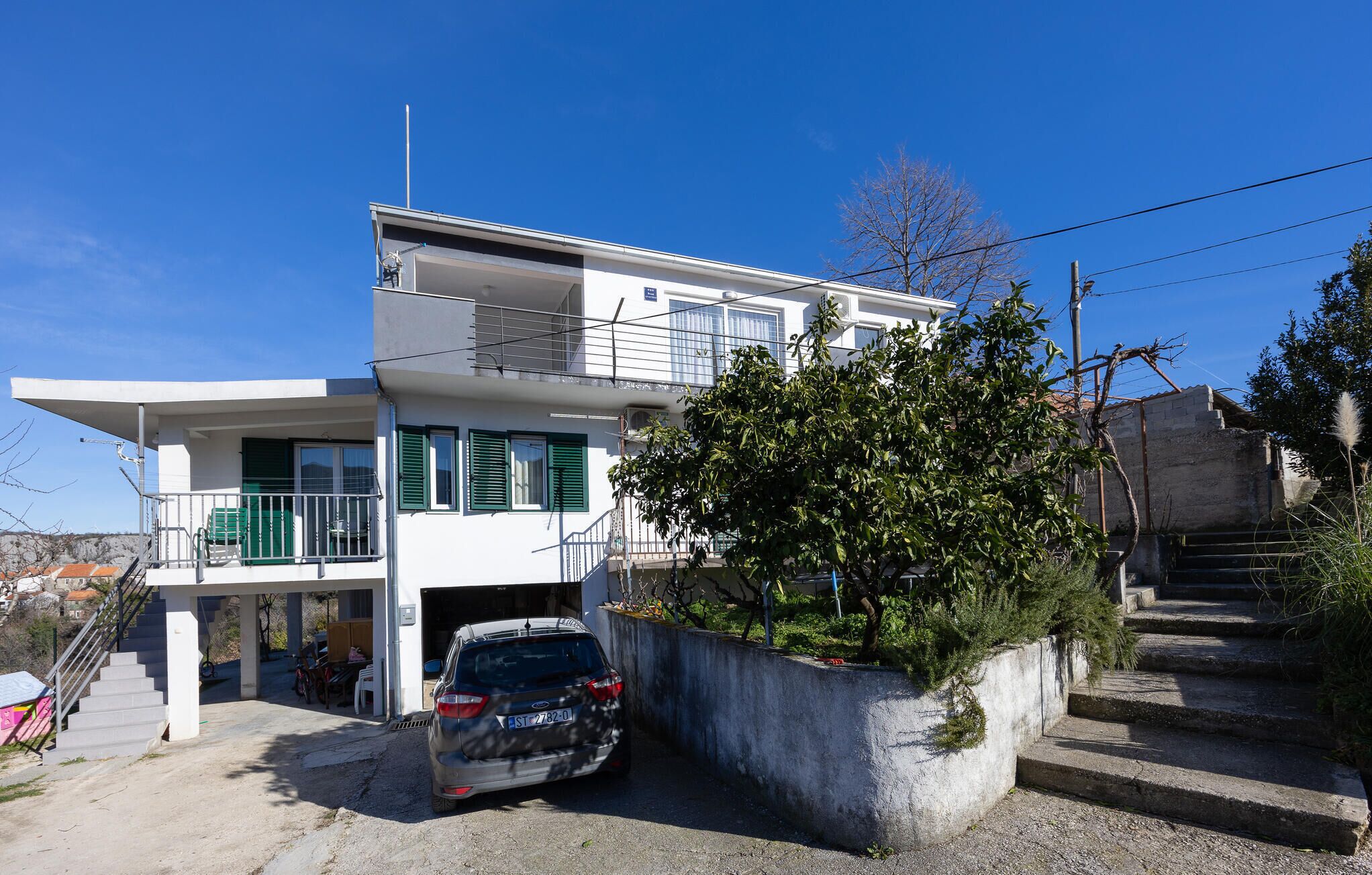 A two-story building with a balcony, a car parked in front, and a staircase leading to the upper level.