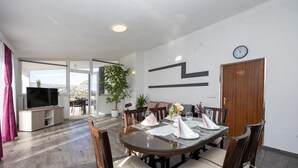 A dining area with a round table set for four, surrounded by wooden chairs with cushioned seats. There is a potted plant on the table, and a clock on the wall. - Gorgeous apartment in Slime (Slime)
