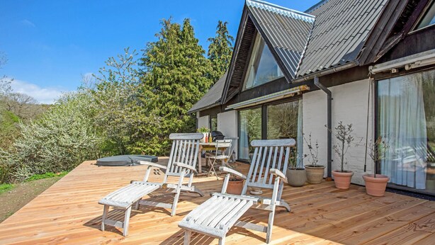A wooden deck with two white chairs and a table, a grill, and potted plants. - Gorgeous apartment in Gudhjem with WiFi (Gudhjem)