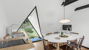 A modern kitchen with a built-in stove, a sink, and a dining area with a round table and wooden chairs. - Gorgeous apartment in Gudhjem with WiFi (Gudhjem)