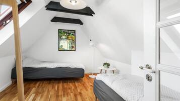 A small, modern bedroom with two beds, a wooden floor, a painting, and a white lamp.