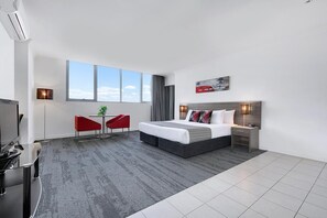 A modern hotel room with a large bed, a desk, a TV, and a window with a cityscape view. - Quest South Brisbane (Brisbane)