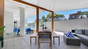 Un patio exterior con mesa y sillas de madera, un sofá y una piscina al fondo.