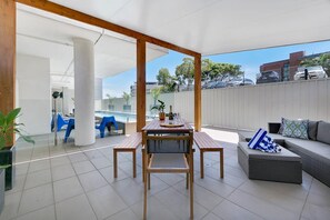 Un espace extérieur aménagé en terrasse, avec une table et des chaises en bois, un canapé et une piscine en arrière-plan.