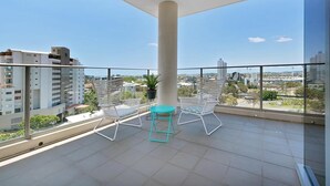Un balcón con vistas despejadas de la ciudad, dos sillas blancas y una mesa turquesa.