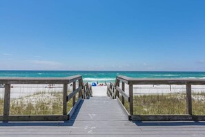 A wooden boardwalk leading to a beach with clear blue water and sandy shore.