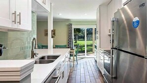 Uma cozinha moderna com eletrodomésticos de aço inoxidável, uma ilha grande e vista para uma área externa verde.