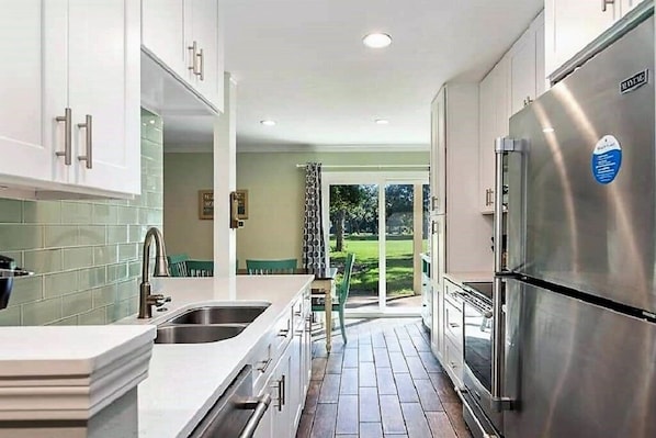 A modern kitchen with stainless steel appliances, a large island, and a view of a green outdoor area.