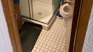 Kylpyhuoneessa on lasiseinällä varustettu suihku, wc ja kuusikulmaisilla laatoilla päällystetty lattia.