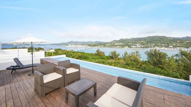 A rooftop pool area with wicker furniture and a view of a bridge and hills.