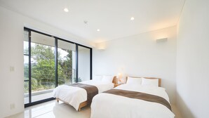 A modern bedroom with two beds, large windows, and a view of greenery outside.