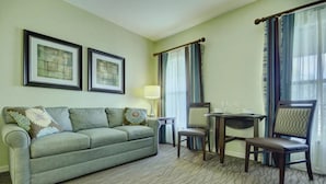 Une chambre d’hôtel avec un canapé, deux fauteuils, une petite table et une lampe.