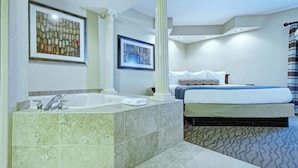 Une chambre d’hôtel avec une grande baignoire, un lit avec de nombreux oreillers et deux tableaux encadrés au mur.
