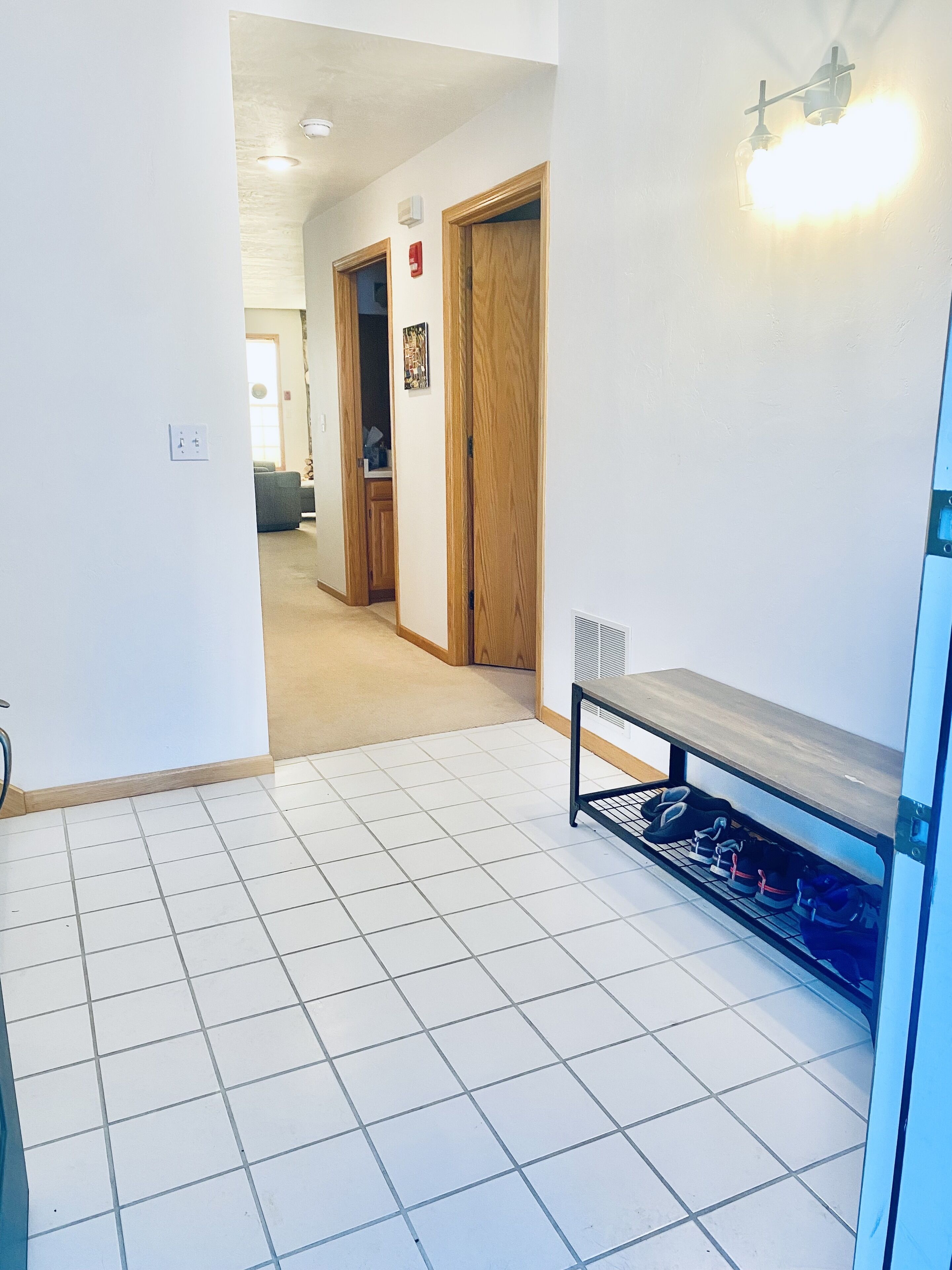 A hallway with a tiled floor, a wooden door, and a shoe rack.