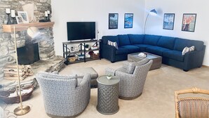 A living room with a stone wall, a dark blue sofa, patterned armchairs, a coffee table, a TV, and a fireplace.