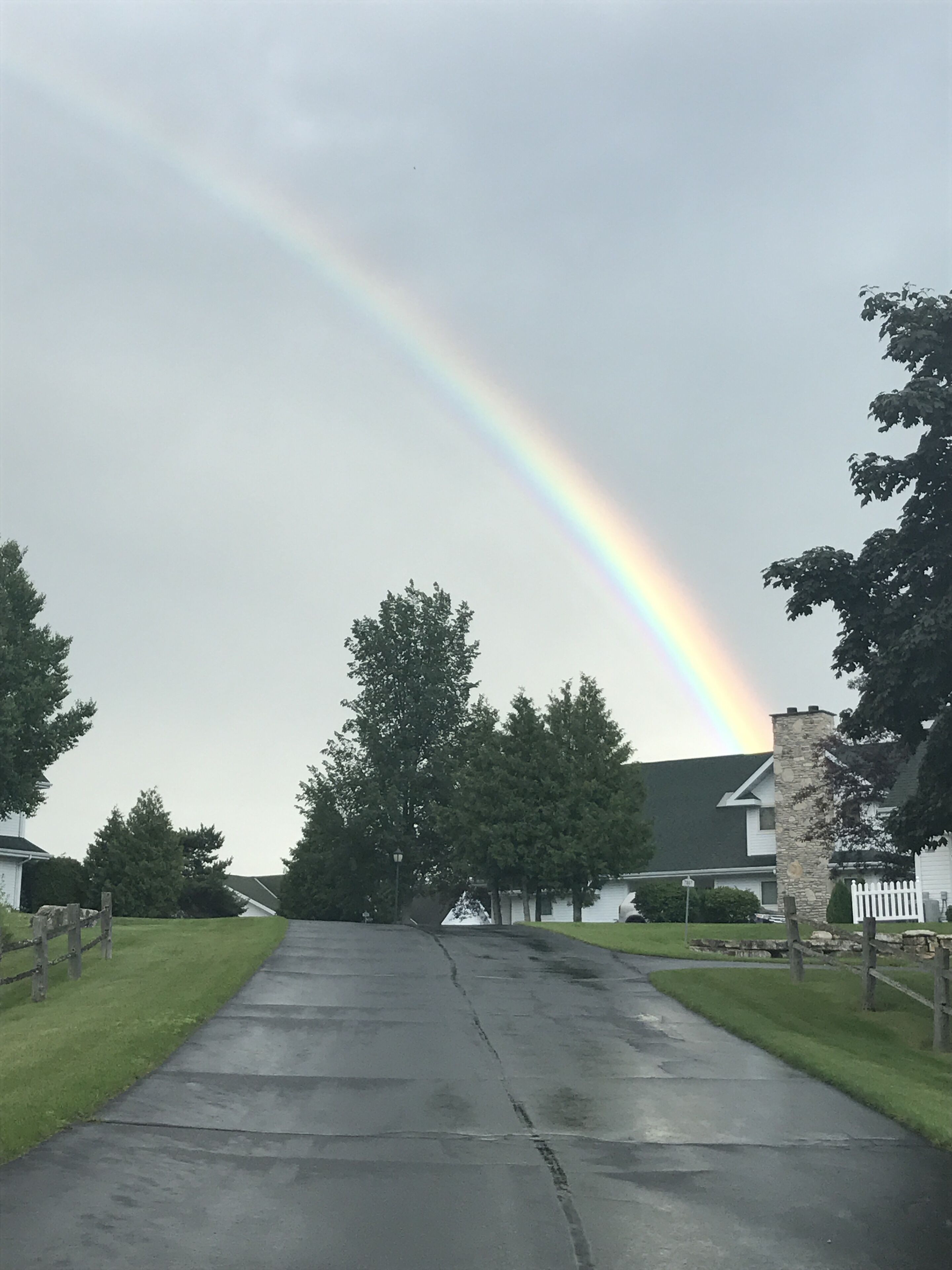 A residential street with houses, a stone wall, and a rainbow in the sky.