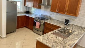 A kitchen with wooden cabinets, a stainless steel refrigerator, a gas stove, and a granite countertop.
