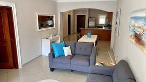 A modern living room with a grey sofa, a small round table, and a kitchen in the background.
