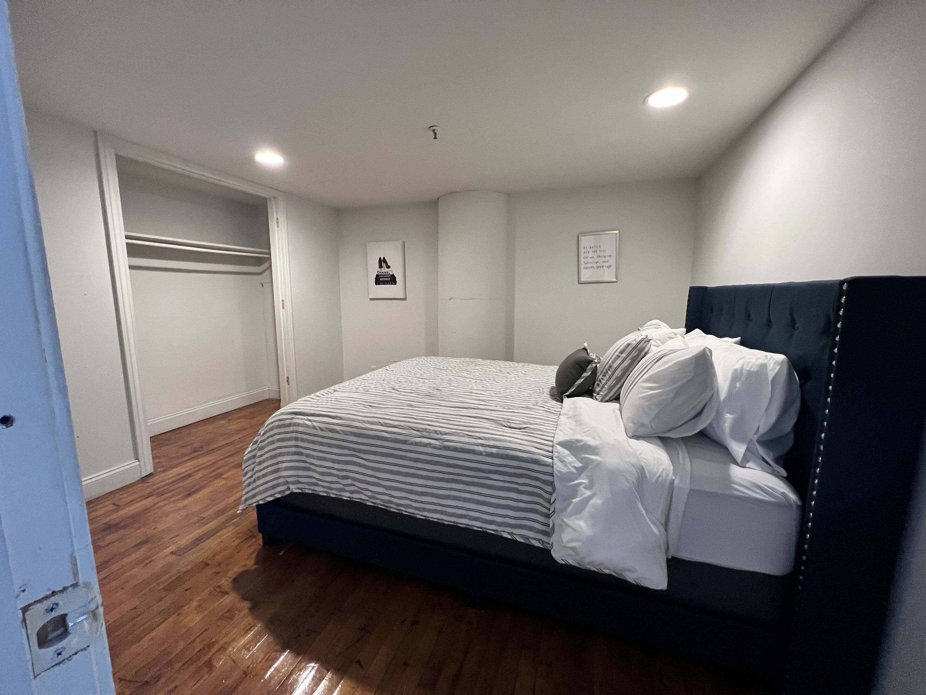 Un dormitorio con una cama, suelo de madera, un armario y dos cuadros en la pared.