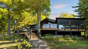 Une maison moderne dotée d’une terrasse en bois, d’un escalier menant à un balcon en verre et d’un chemin en pierre.